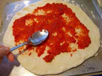 spreading the tomato sauce on the pizza base